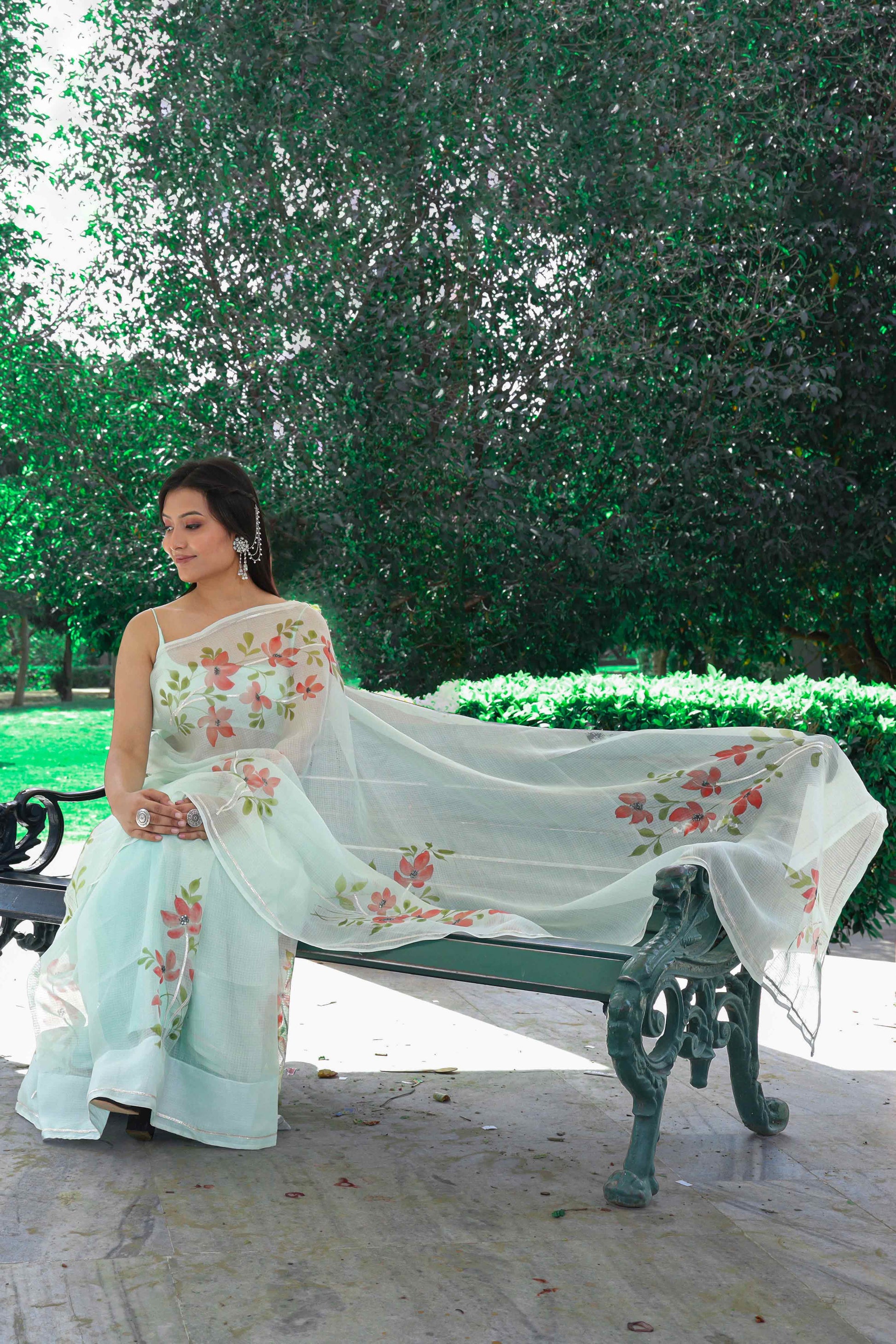 A stunning green Kota Doria saree adorned with hand-painted red flowers and embellished with sequins and gota embroidery. Perfect for silk saree blouse designs, hot saree styles, and the latest saree blouse designs in 2022. Ideal for saree enthusiasts looking for a simple yet elegant look. This hand-painted saree is a work of art, making it a great choice for engagement and party looks. Explore the best saree shop near you for this pure Kota silk masterpiece