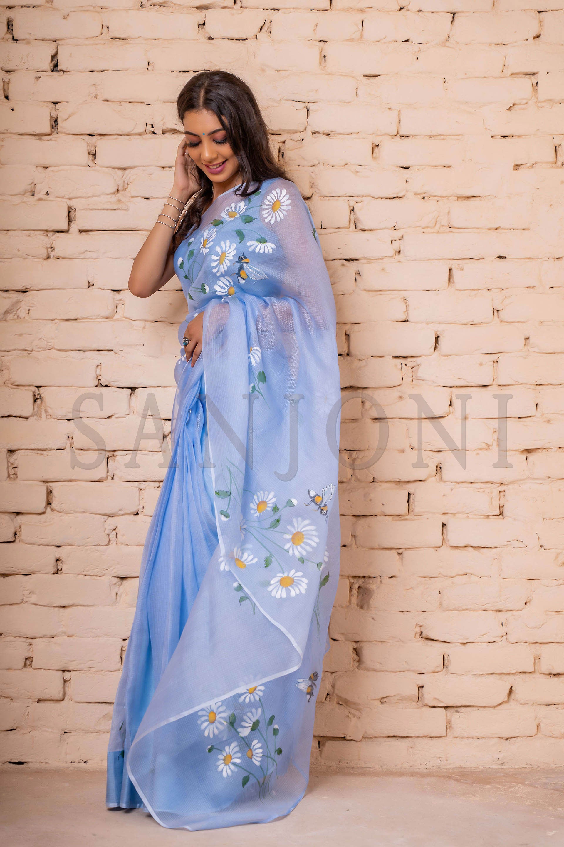 Exquisite hand-painted Kota Doria Silk Saree adorned with delicate white daisies, intricately enhanced with sequin and gota hand embroidery. A masterpiece of hand painting on saree, showcasing the elegance of pure Kota silk. This Kota saree is a timeless beauty that epitomizes artistry and grace.