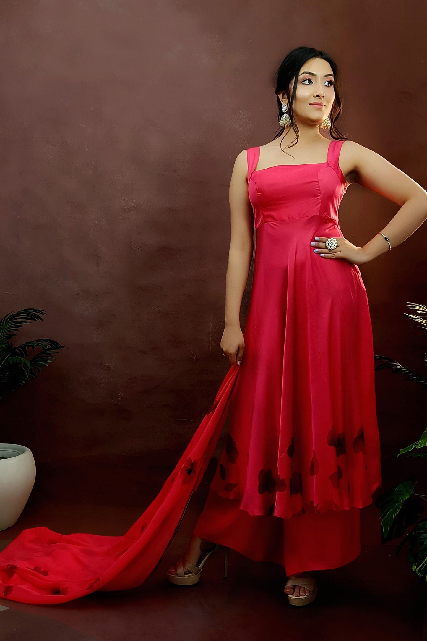 Girl wearing a red colour sleeveless anarkali suit enhanced with hand painted black poppy flowers adorned with delicate bead work., paired with organza handpainted dupatta and a flared palazzo.