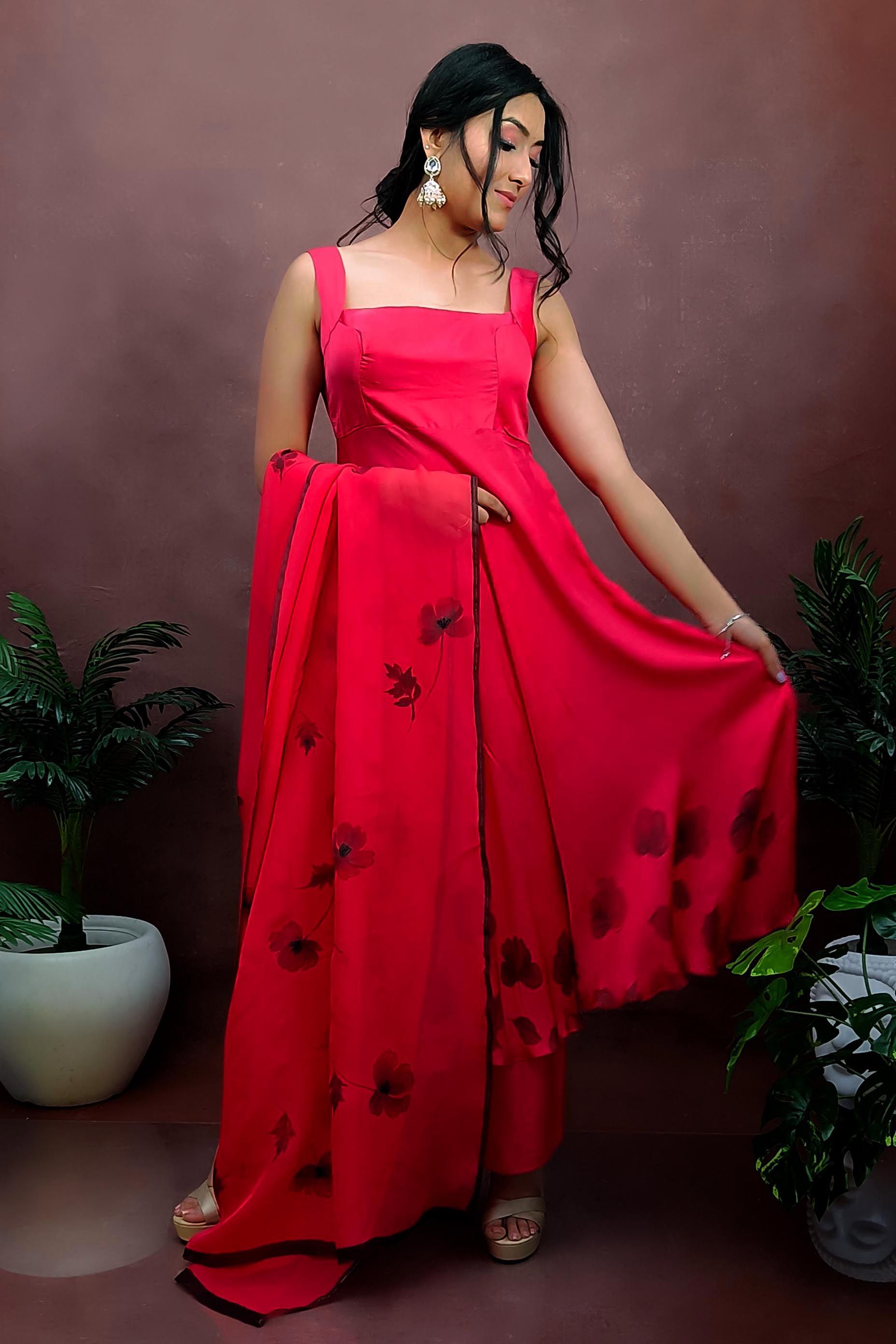 Girl wearing a red colour sleeveless anarkali suit enhanced with hand painted black poppy flowers adorned with delicate bead work., paired with organza handpainted dupatta and a flared palazzo.