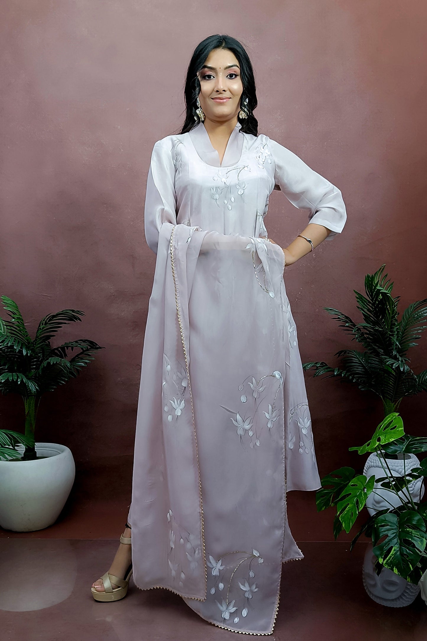Girl is wearing Hand-painted A-line suit in light move color silk , white color fuchsia flowers enhanced with sequin and gota embroidery, paitred with an organza dupatta and straight pants.