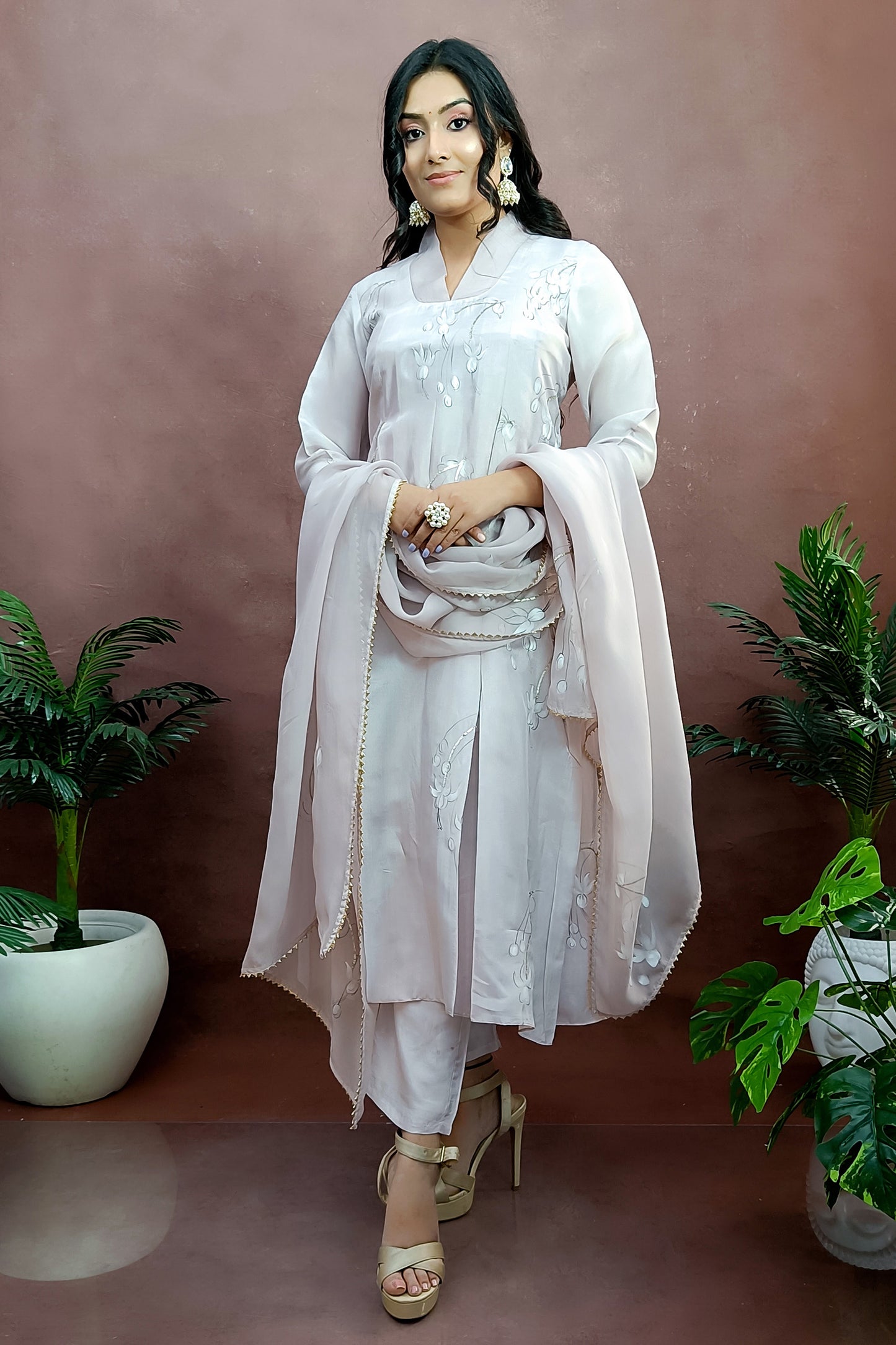Girl is wearing Hand-painted A-line suit in light move color silk , white color fuchsia flowers enhanced with sequin and gota embroidery, paitred with an organza dupatta and straight pants.