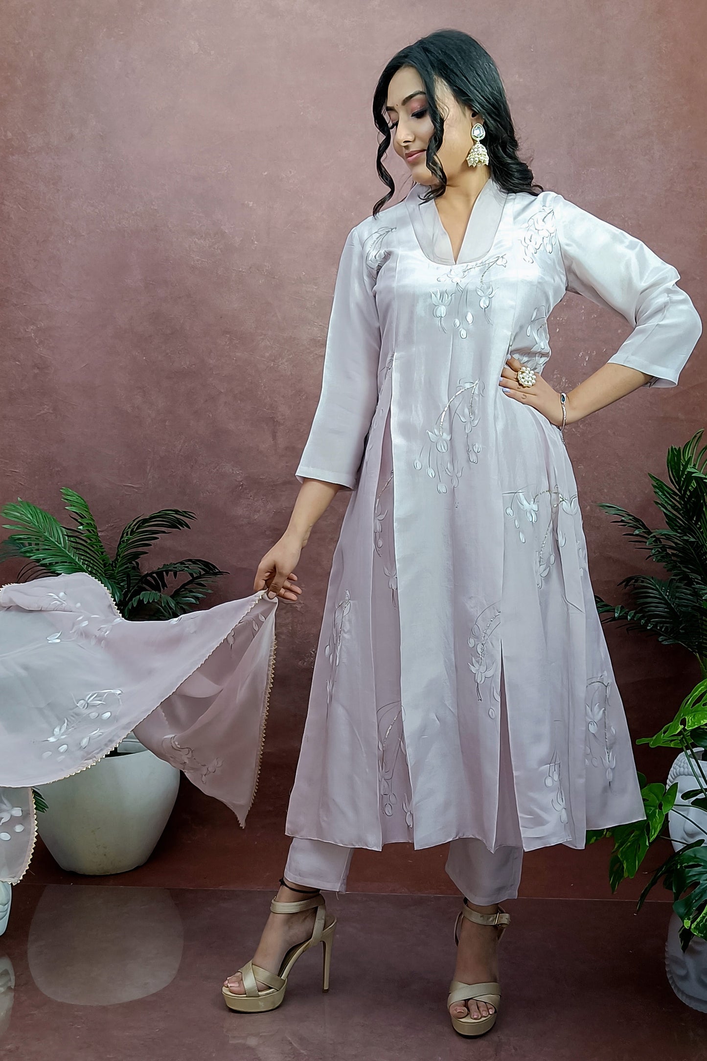 Girl is wearing Hand-painted A-line suit in light move color silk , white color fuchsia flowers enhanced with sequin and gota embroidery, paitred with an organza dupatta and straight pants.