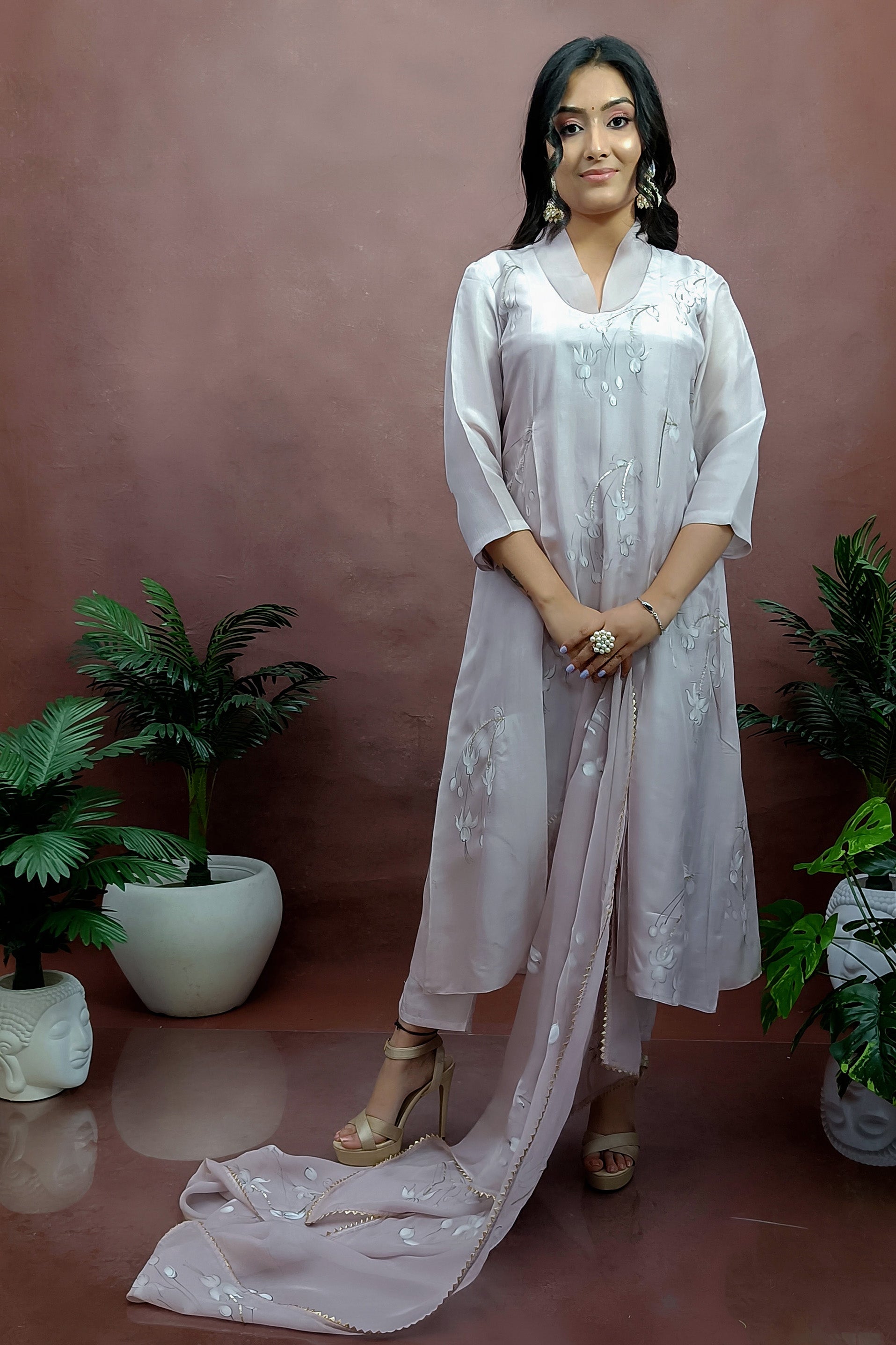Girl is wearing Hand-painted A-line suit in light move color silk , white color fuchsia flowers enhanced with sequin  and gota embroidery, paitred with an organza dupatta and straight pants.