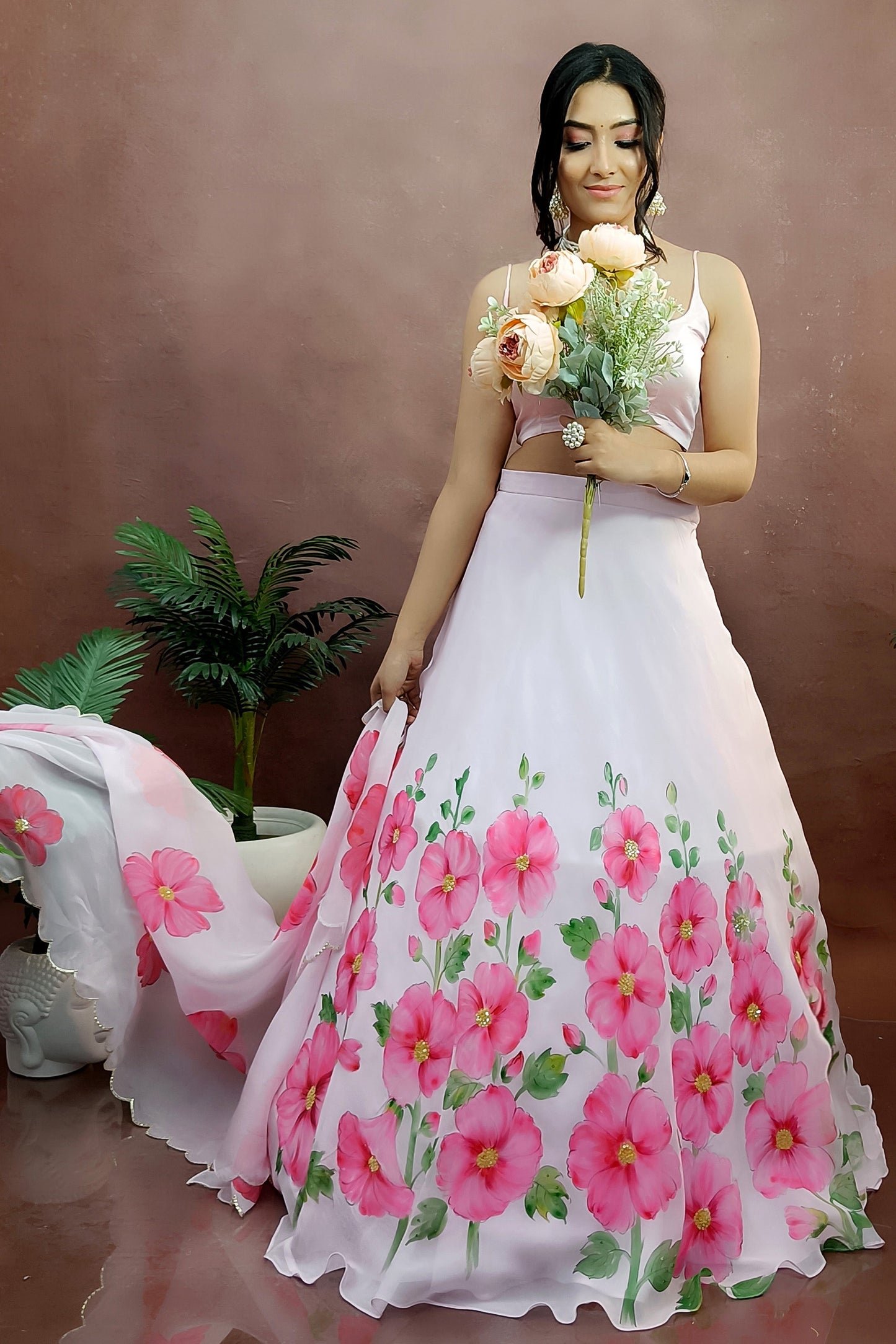 Hand painted hollyhocks on baby pink organza lehenga paired with an organza  painted dupatta enhanced with sequin embroidery and gota scalloping.