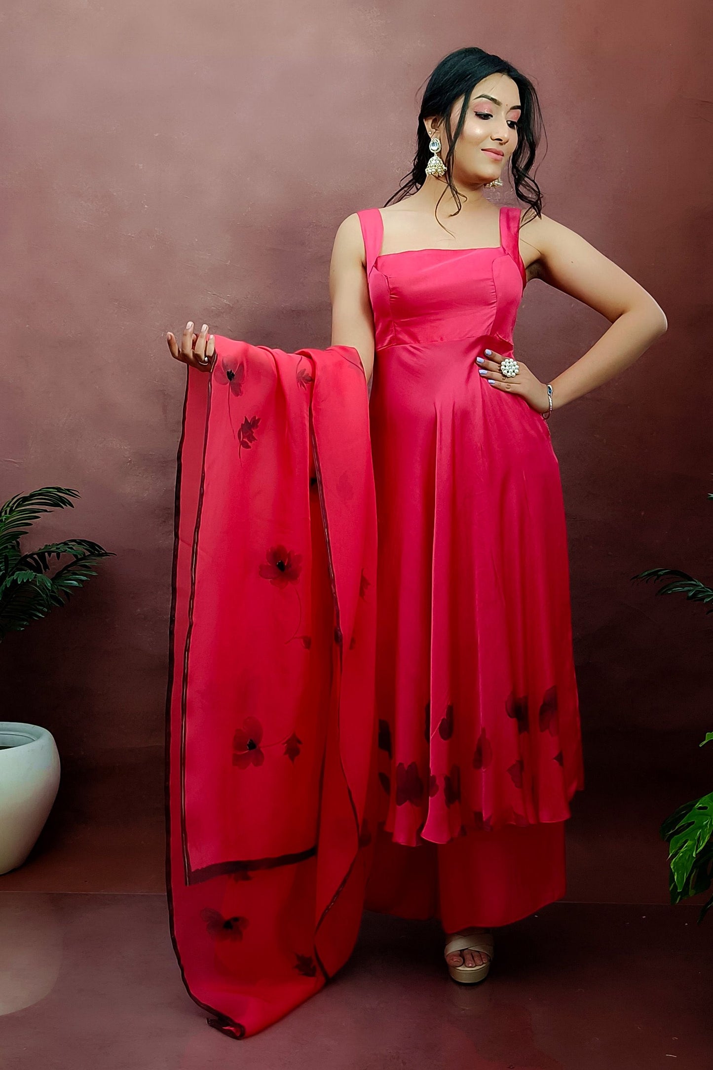 Girl wearing a red colour sleeveless anarkali suit enhanced with hand painted black poppy flowers adorned with delicate bead work., paired with organza handpainted dupatta and a flared palazzo.