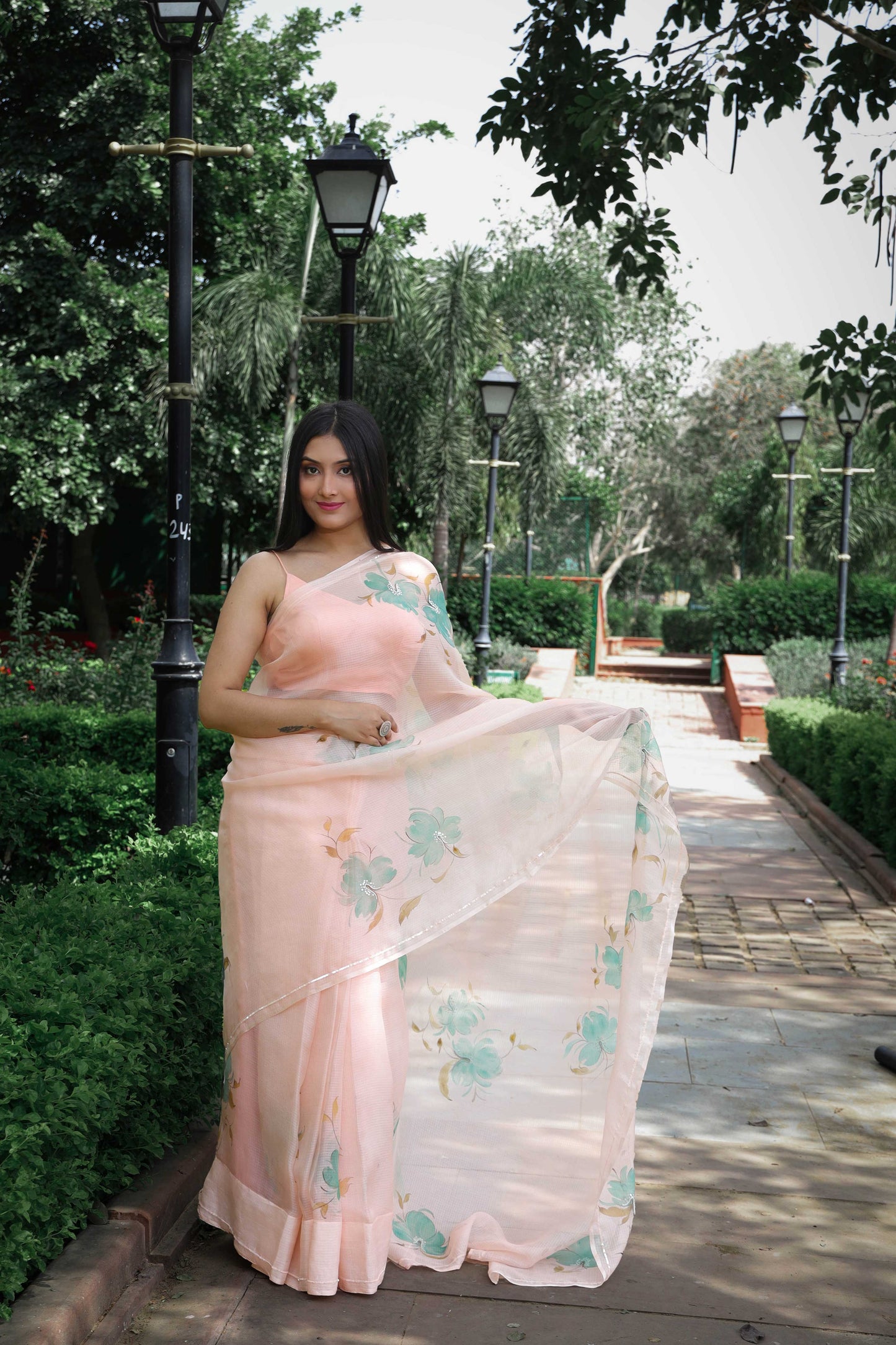 Graceful hand-painted Kota Doria Silk Saree in light peach, adorned with green floral motifs, and beautifully enhanced with sequin and pearl hand embroidery. A true masterpiece of hand painting on saree, showcasing the timeless beauty of pure Kota silk