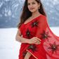 Woman wearing a red saree with black floral patterns against a snowy mountain background