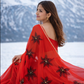 Woman in a red saree with floral patterns standing in a snowy landscape.