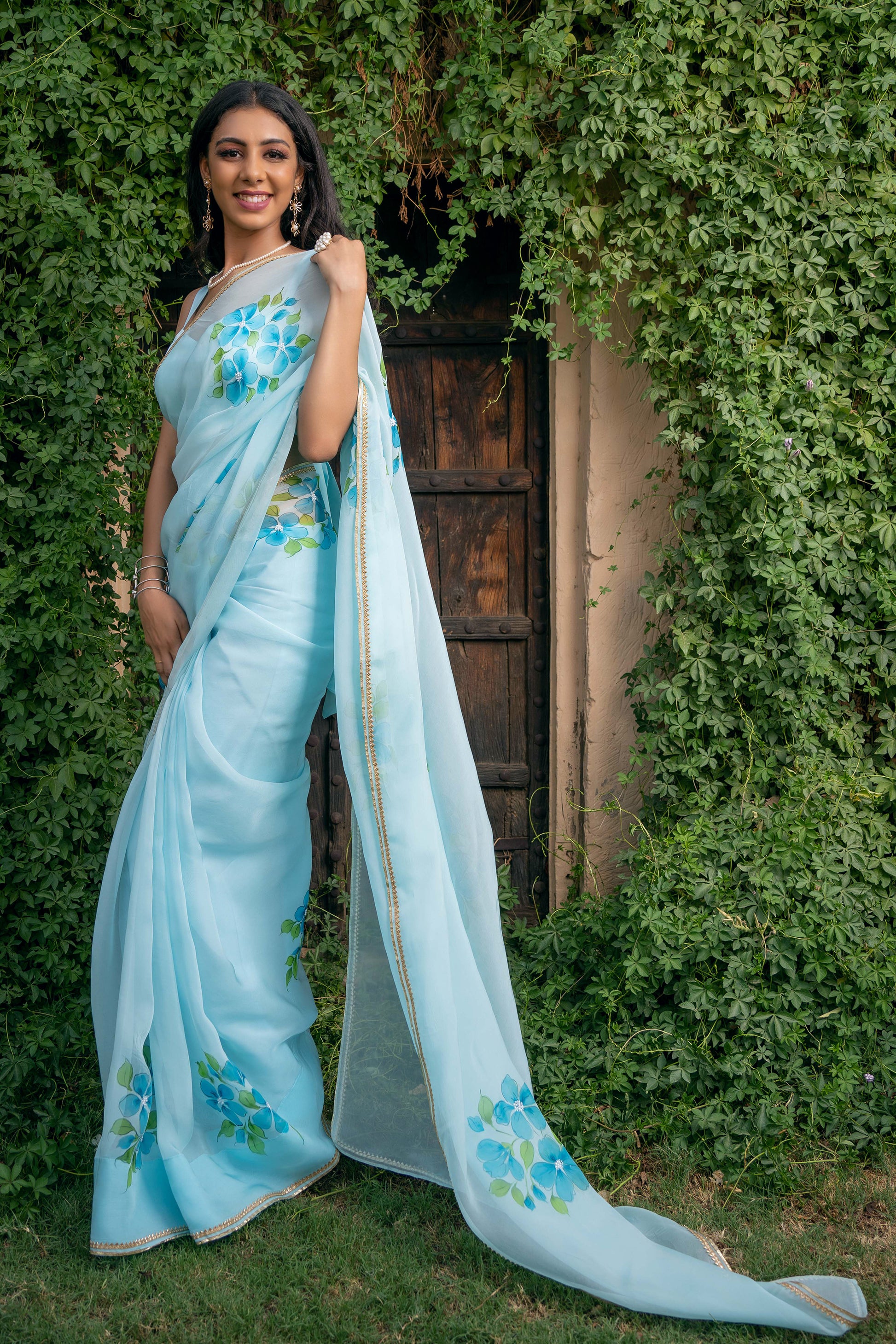 Capture the essence of elegance with this light turquoise Plumeria hand-painted organza saree from our latest collection. This handwork saree is the most popular and trending saree designs. Complete with a stitched blouse, this fancy organza saree is a testament to timeless beauty, reminiscent of Bollywood and Sabyasachi styles. Elevate your wardrobe with this beautiful handloom saree, the epitome of sophistication and grace, now available in our latest design series